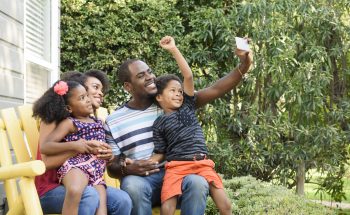 A mother and father with their son and daughter sitting on a bench outside.
