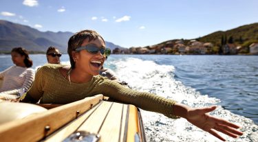 A woman on a boat with 2 others extends her hand over the water with a big smile