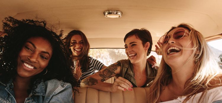 Four female friends smile and laugh during a road trip.