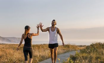 A man and a woman in workout gear high five in a field by the ocean.