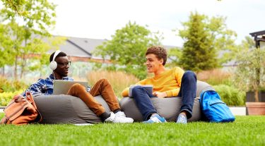 2 students lounge on bean bag chairs in the grass