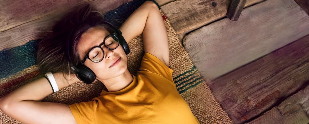 A woman with glasses relaxes with her hands behind her head and her eyes closed