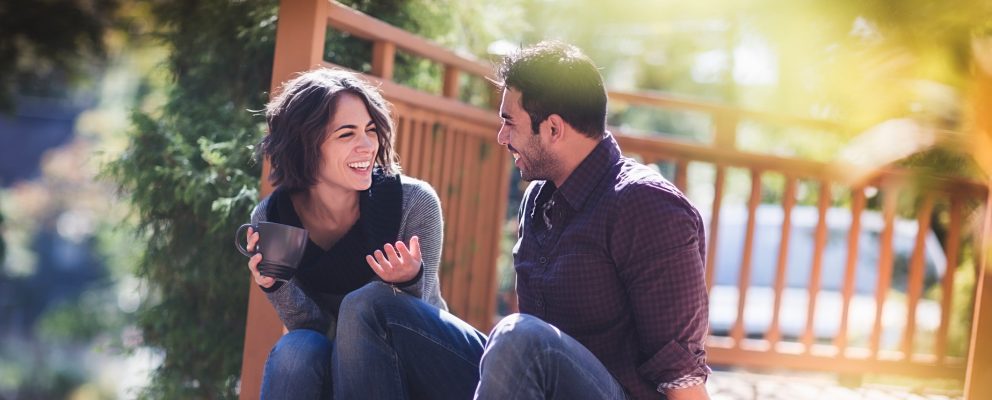 A man and a woman sit on a bench laughing.