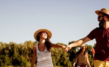 A couple holds hands as they walk in the sun with friends
