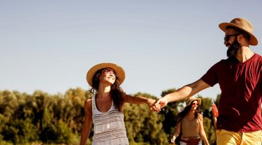 A couple holds hands as they walk in the sun with friends