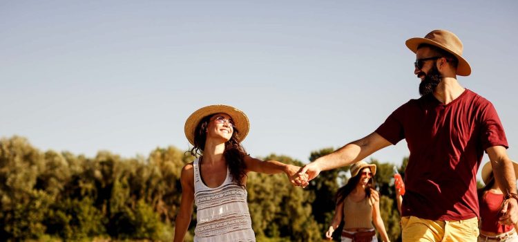 A couple holds hands as they walk in the sun with friends