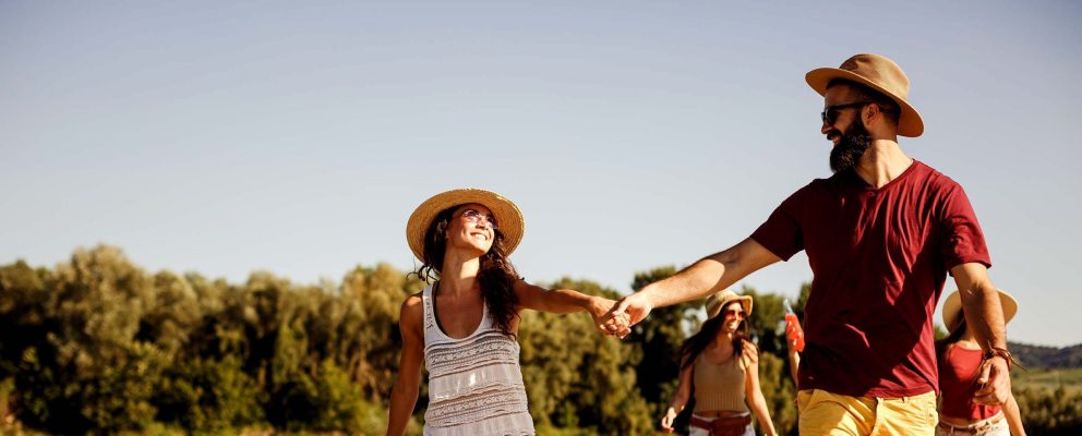 A couple holds hands as they walk in the sun with friends