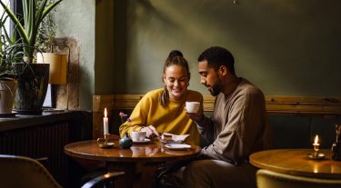 A couple at a café share a desert and drink coffee.