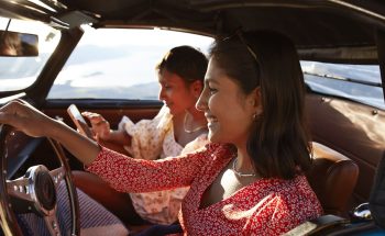 Woman driving a car while another woman sits in the passenger seat on her phone.
