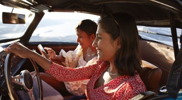 Woman driving a car while another woman sits in the passenger seat on her phone.