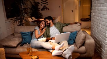 A couple relaxes on a couch with their feet up and laugh