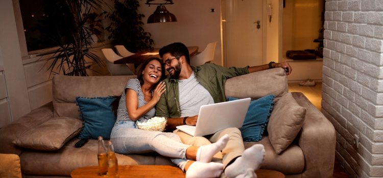 A couple relaxes on a couch with their feet up and laugh
